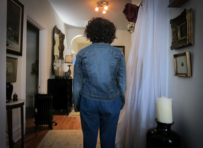 Model' back is facing the camera wearing a dark jean jacket with no daisies. The jacket reaches her hips. This is the before picture.