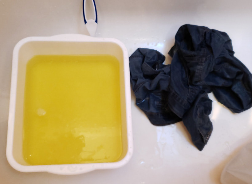 Left to right: the bucket filled with excess dye (a light yellow colour). The dark jacket now wet, crumpled and a slightly lighter shade.