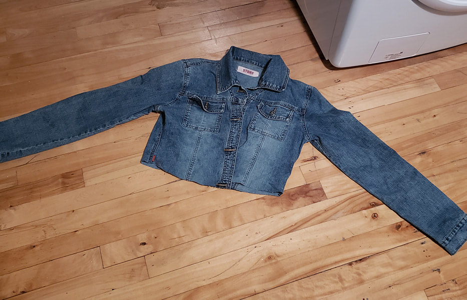 The jacket laying flat on the floor, fully dried and a lighter shade of blue. The bottom has been cut off, it is shorter now.