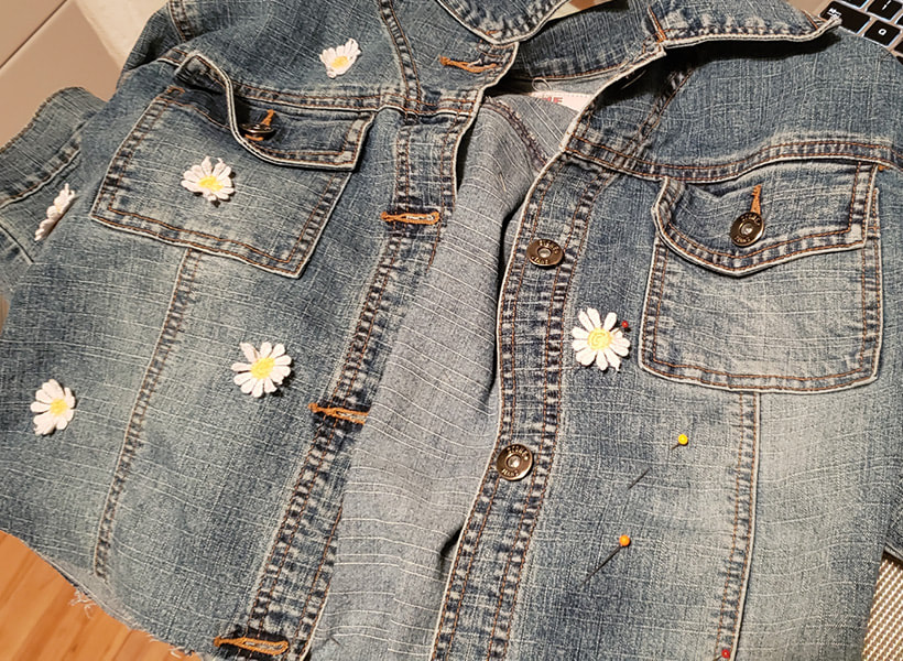 Closeup of the jacket with daisies placed randomly on it. Pins hold some of the daisies to the jacket.