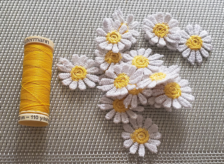 Left to right: spool of yellow thread. small pile of daisy appliqués.